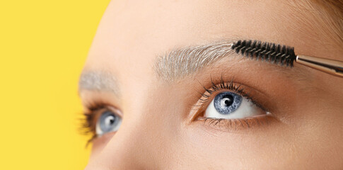 Young woman with dyed eyebrows and brush on color background, closeup