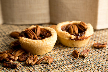 Pecan tarts with loose pecans lying on a woven mat