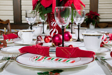 a Christmas table place setting with red ornaments and a red napkin in a silver napkin ring

