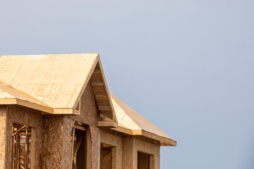 A residential frame house construction project showing the engineered truss roof rafters and oriented strand chip board engineered wall sheathing