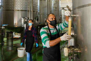 Man worker of winery in protective mask checking wine production process at fermentation tank