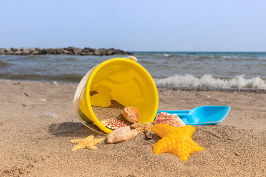 a yellow child's toy plastic pail on beach sand surrounded by seashells and a starfish