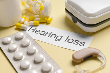Paper with text HEARING LOSS, aid and pills on color background