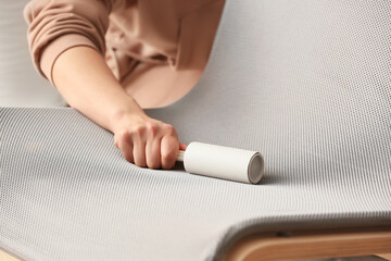 Woman cleaning armchair with lint roller, closeup