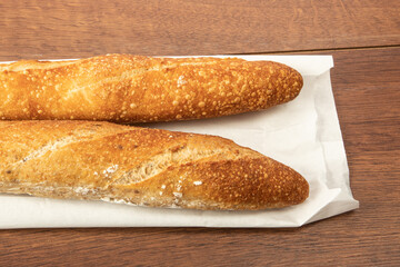 Two bread French sticks or baguettes on a white paper bag on a wooden table background