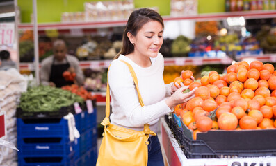 Smiling female customer picking fresh tomatoes in shop