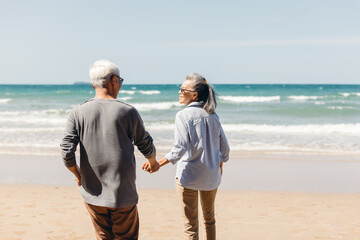 Retired couple holding hand happily walked down to the sandy beach. An elderly wife holding her husband's hand and smile happily. Plan life insurance and retirement concept..