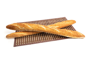 Two crossed crusty bread French sticks or baguettes on a wooden mat isolated on white
