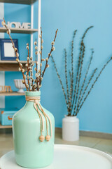 Vase with willow branches on table in room