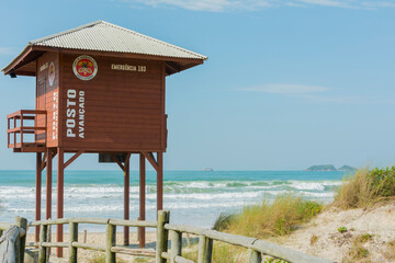 Wooden boardwalk on the beach with lifeguard tower on an empty beach with clear sand and blue sea in southern Brazil. Lifeguard station. Safety concept.