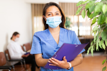 Portrait of confident woman healthcare worker wearing medical face mask for disease protection standing in clinic office, meeting patients