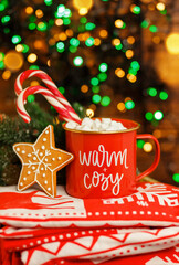 Hot chocolate with marshmallows and candy stick. Cup of tasty cocoa with Xmas candy cane on wooden table against blurred festive lights.Traditional beverage for winter time. Mug with Christmas decor.