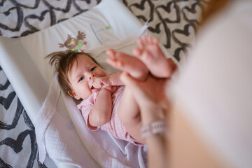 Happy caucasian baby four months old lying on the bed happy while unknown parent mother is cleaning...