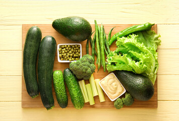 Board with different green vegetables on color wooden background