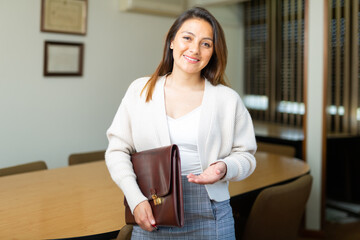 Positive smiling latino american business woman with briefcase standing in her office