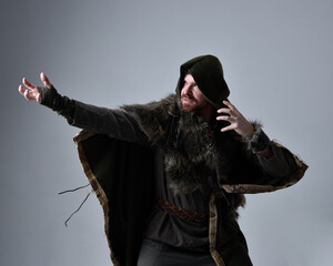 Close up  portrait of  young handsome man  wearing  medieval Celtic adventurer costume with hooded fur cloak,  isolated on studio background.