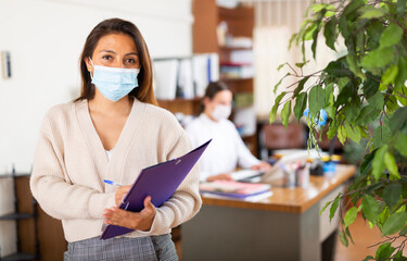 Portrait of hispanic business woman in face mask standing in modern office interior