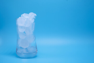 Close-up shot, showing the ice in clear glass of water melting on copy space blue background as the temperature rises. Media about global warming from world climate change and the greenhouse effect.
