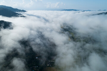 Fototapeta na wymiar Aerial view drone shot of flowing fog waves on mountain tropical rainforest,Bird eye view image over the clouds Amazing nature background with clouds and mountain peaks in Nan Thailand.
