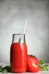 Bottle of tasty tomato juice on grey background