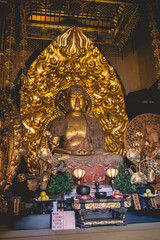 Golden seated buddha sculpture (lotus pose) and other art pieces in a altar at a buddhist temple in Kamakura, Japan