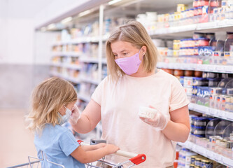 Mother and her little daughter wearing protective face mask shop a food at a supermarket during the coronavirus epidemic or flu outbreak