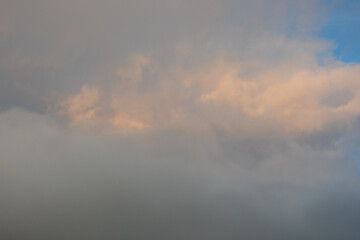 Blue-gray clouds in the sky illuminated by the setting sun. Light blue sky behind dark and dramatic storm clouds. Perfect natural sky background, mock up for design