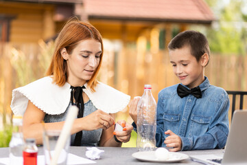Mom and son are doing physical experiments at home. An experience with a child on how to place a boiled egg in the narrow neck of a plastic bottle using fire. Homemade creativity with a child