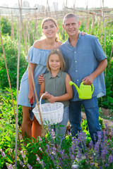 Family of three people standing in kitchen garden and smiling.