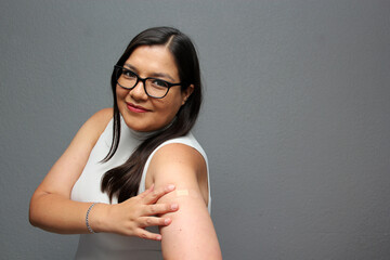 Happy Latina adult woman shows her arm that just received the Covid-19 vaccine in the new normal...