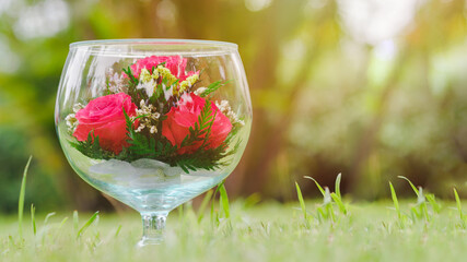 Crystal wine glasses are large, decorated with a red rose on the meadow with beautiful lighting fair. Coppy space. Gift ideas for lovers.