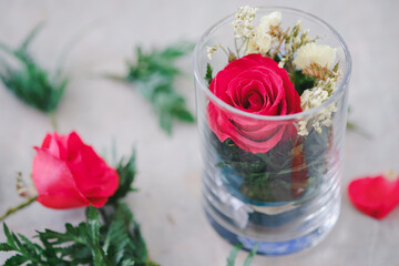 Red roses and decorative leaves in glass are beautifully arranged on the table. Gift ideas for lovers.