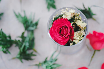 Red roses and decorative leaves in glass are beautifully arranged on the table. Gift ideas for lovers. Top view.