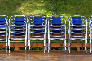 Fototapeta na wymiar Metal chairs stacked in piles, and next to a beach umbrella in a street restaurant, cafe or recreation center. The chairs are on the wooden floor. Resorts are waiting for tourists and visitors