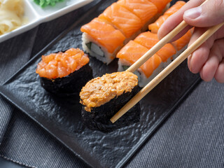 a variety of Japanese rolls and sushi on a textured black plate. Side view. Bamboo sticks hold one gunkan. Close up