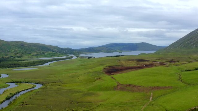 Failmore River, Maum, Connemara, County Galway, Ireland, July 2021. Drone slowly tracks north over grassy marshland with Lough Corrib in the distance.