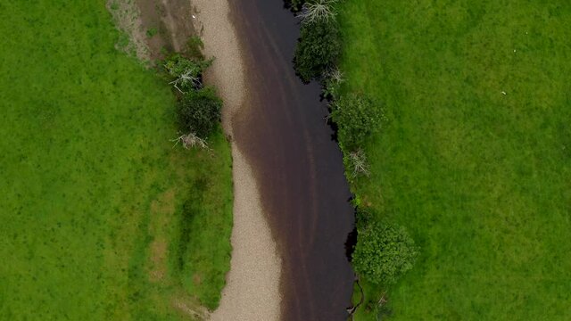Failmore River, Maum, Connemara, County Galway, Ireland, July 2021. Drone Bird's eye view, slowly following the course of the river west over grassy marshland revealing a crossing bridge.