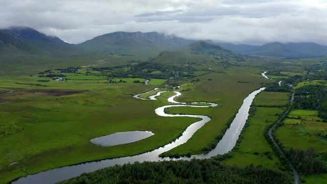 Failmore River, Maum, Connemara, County Galway, Ireland, July 2021. Drone gradually ascends while facing west, revealing vista of winding river with Oxbow Lake and grassy marshland.