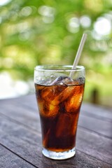 Cola drink on a wooden table and the blur background of green plant.
