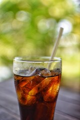 Cola drink on a wooden table and the blur background of green plant.