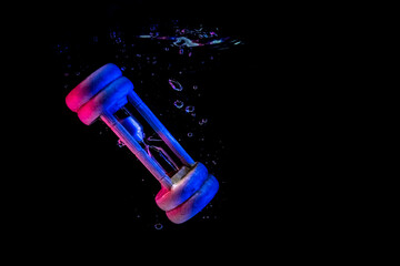 Creative Underwater photo of hourglass or sandglass, drowning in the water. Black background