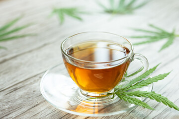 Glass cup of cannabis herbal tea. Cup of tea with marijuana and fresh green leaves on the wooden background.