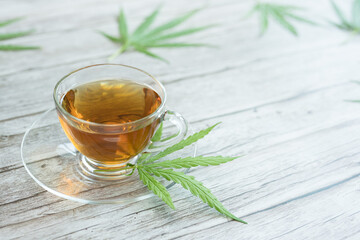 Glass cup of cannabis herbal tea. Cup of tea with marijuana and fresh green leaves on the wooden background.