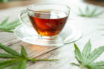 Glass cup of cannabis herbal tea. Cup of tea with marijuana and fresh green leaves on the wooden background.