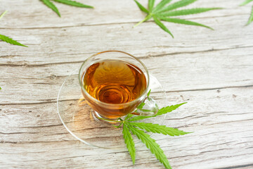 Glass cup of cannabis herbal tea. Cup of tea with marijuana and fresh green leaves on the wooden background.