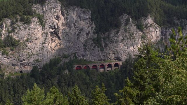 Train running through tunnel on side of rocky cliff at Semmering Railway in Austria