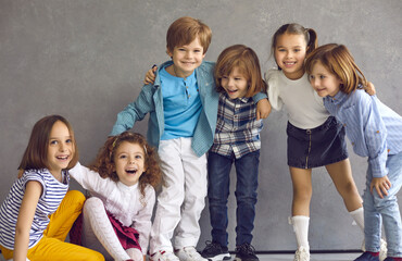 Boys and girls having fun. Group portrait happy friends standing or sitting on floor near studio wall. Team of positive active children in comfortable kids wear hugging, laughing and looking at camera