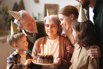 Happy senior woman holding cake with burning candles while celebrating birthday with big lovely...