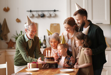 Cute excited little child making wish, blowing candles on cake while celebrating Birthday with family