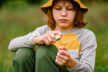 Young male tourist applying insect repellent on hands during hiking trip in forest